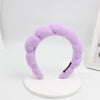 A purple sponge terry cloth headband for hair styling displayed on a white stand.