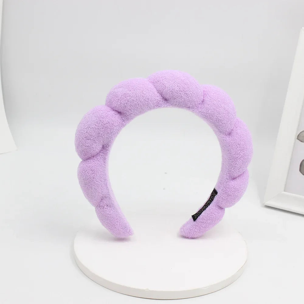 A purple sponge terry cloth headband for hair styling displayed on a white stand.