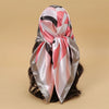 A pink, black, and silver satin square scarf tied in a bow, suitable for hijab or hair.
