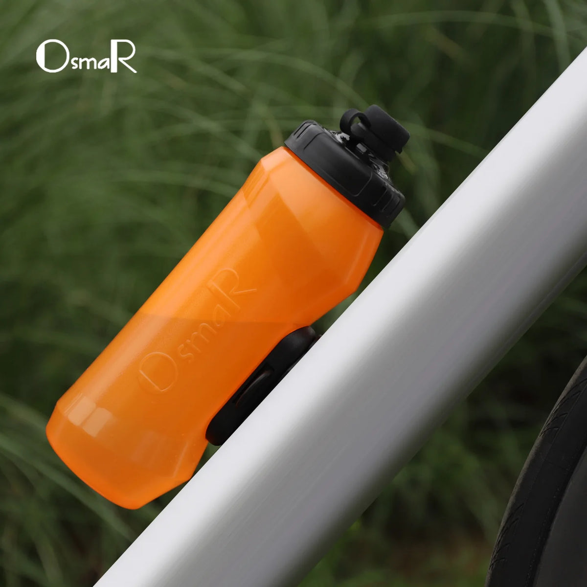 An orange magnetic quick-release bicycle water bottle is shown against a blurred green background.
