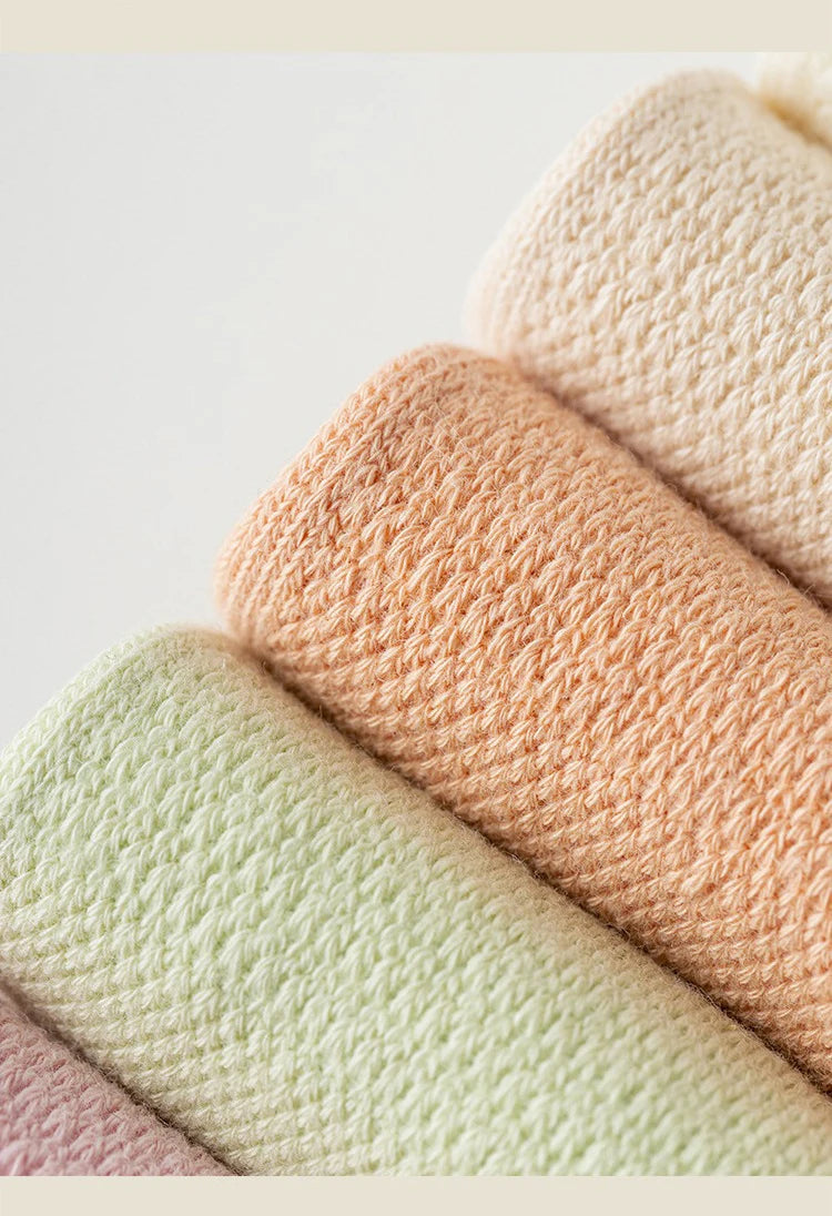 A stack of four pastel colored non-slip yoga socks in peach, pale green, and pink tones.