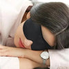 A woman is wearing a black light blocking sleep mask while resting her eyes, with a pink garment visible.