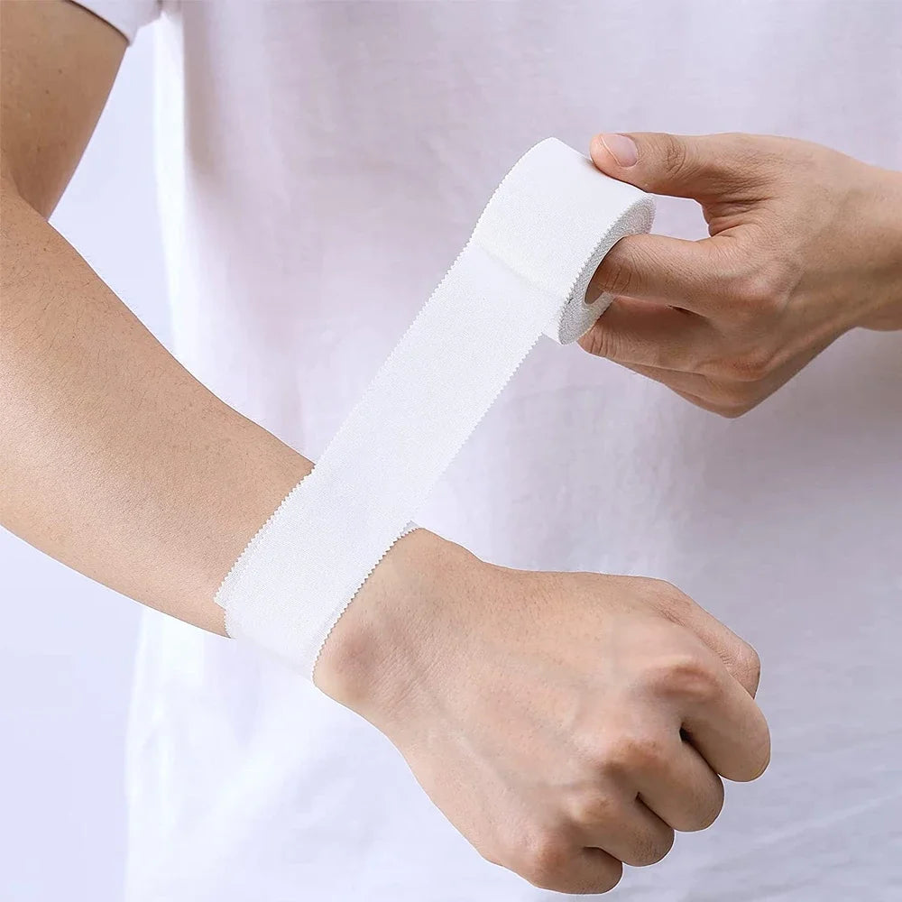 A hand is applying white athletic binding tape around a wrist for sports injury support.