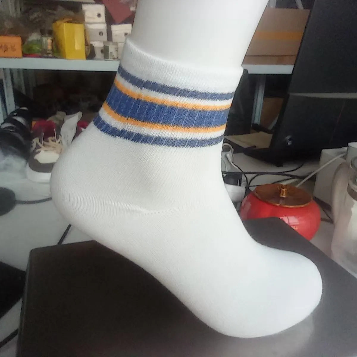 A close-up of a white sock with blue and orange stripes displayed on a dark surface.