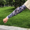 A person's arm displaying a black and white floral tattoo sleeve is resting on green grass.