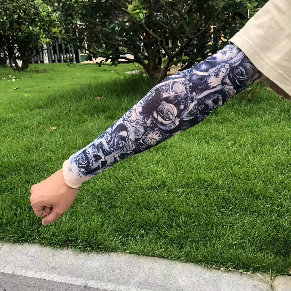A person's arm displaying a black and white floral tattoo sleeve is resting on green grass.