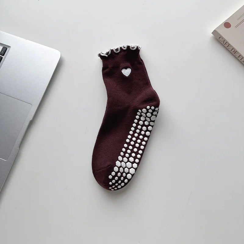 A pair of dark brown yoga socks with silver embroidery and white polka dots resting on a white surface.