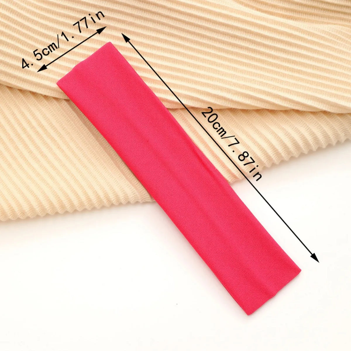 A bright pink stretchable cotton sweat absorbing headband is shown lying on a beige ribbed fabric with dimension markings.
