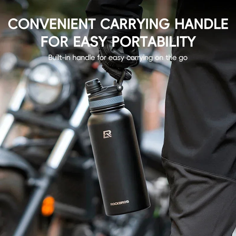 A black insulated stainless steel thermal water bottle with a convenient carrying handle is shown being held by a person near