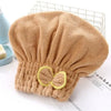 A fluffy, beige hair drying towel cap with a decorative bow is shown on a white surface.