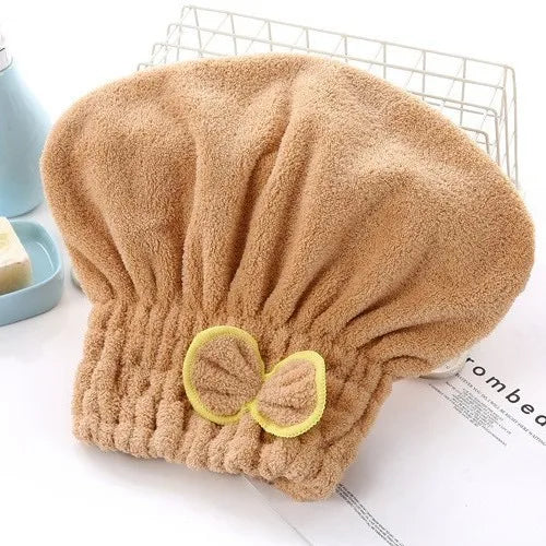 A fluffy, beige hair drying towel cap with a decorative bow is shown on a white surface.