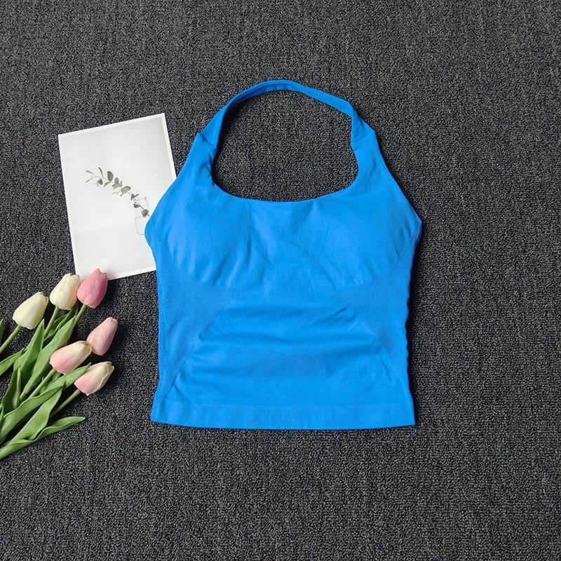 A bright blue seamless yoga and pilates sports bra is displayed on a dark gray fabric next to some pink tulips and a white ca