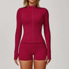 A woman wearing a long-sleeved maroon yoga sports set consisting of a zip-neck top and matching shorts.
