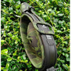 A black collapsible silicone camping kettle with a camouflage green sleeve is shown outdoors among green foliage.