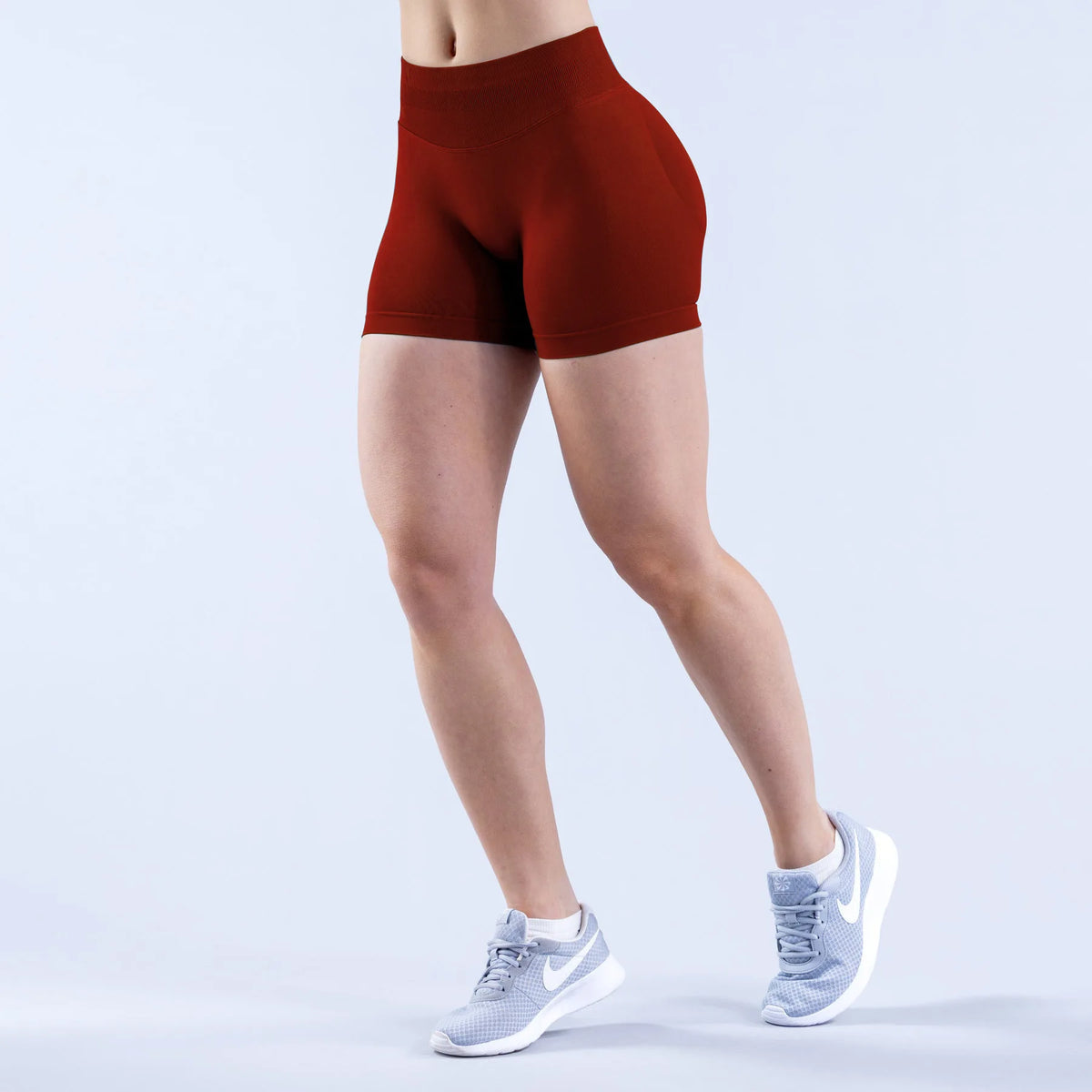 A person is wearing a terracotta red seamless high-waisted yoga short and white athletic shoes.
