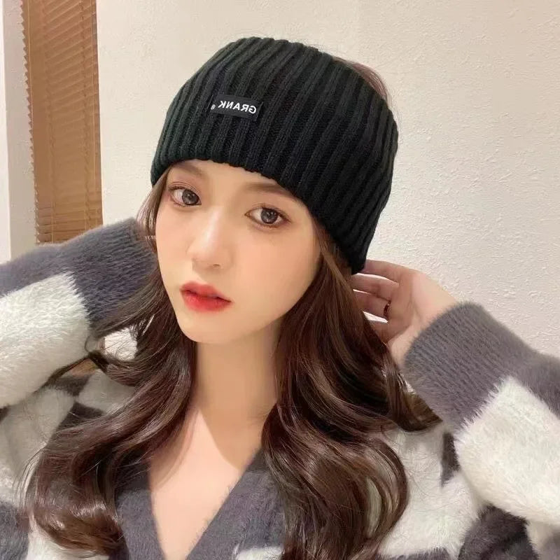 A woman wearing a black knitted headband and a gray and white patterned sweater.