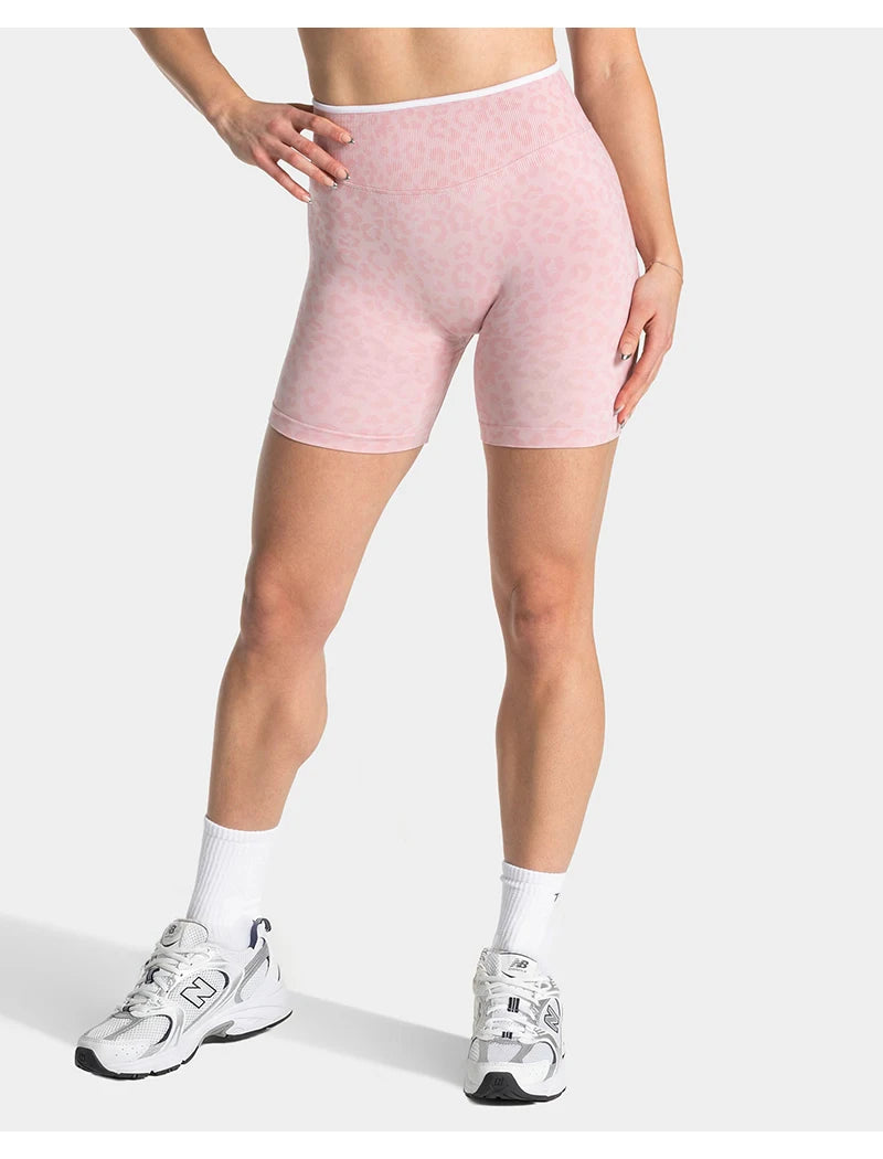Pink leopard print seamless yoga shorts worn by a model, paired with white socks and athletic shoes.