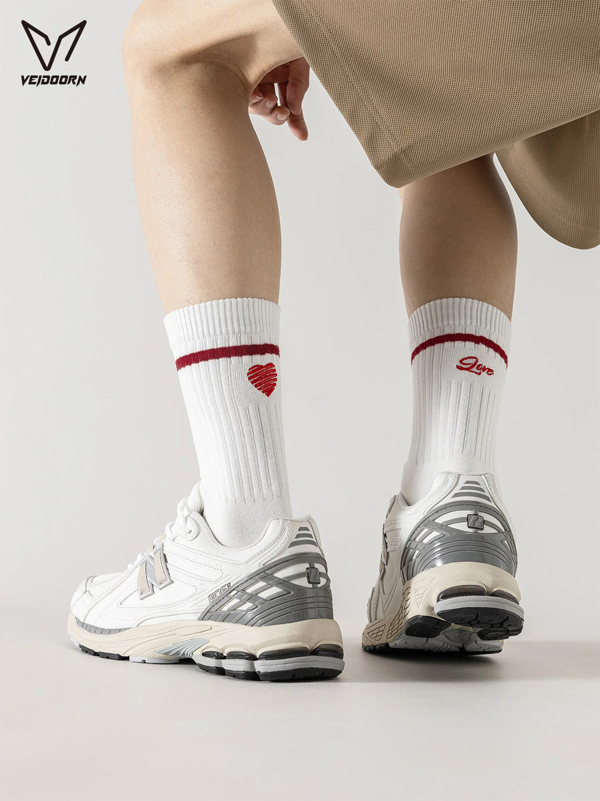 A pair of white crew socks with a red heart detail are worn with light beige pants and white athletic shoes.