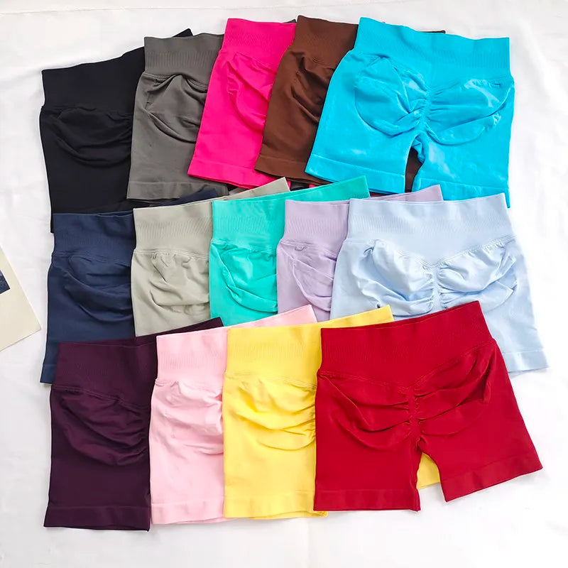 Collection de shorts de yoga sans couture à taille haute dans diverses couleurs vives et sourdes, disposés sur une surface bl