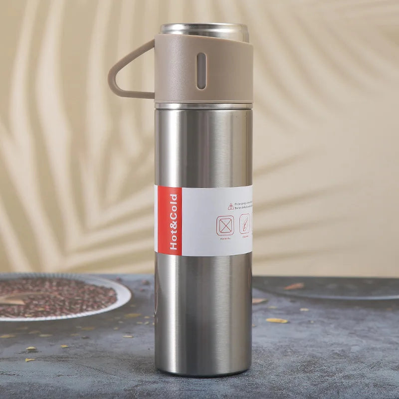 A stainless steel vacuum flask with a handle and a colored label is shown standing on a dark surface.