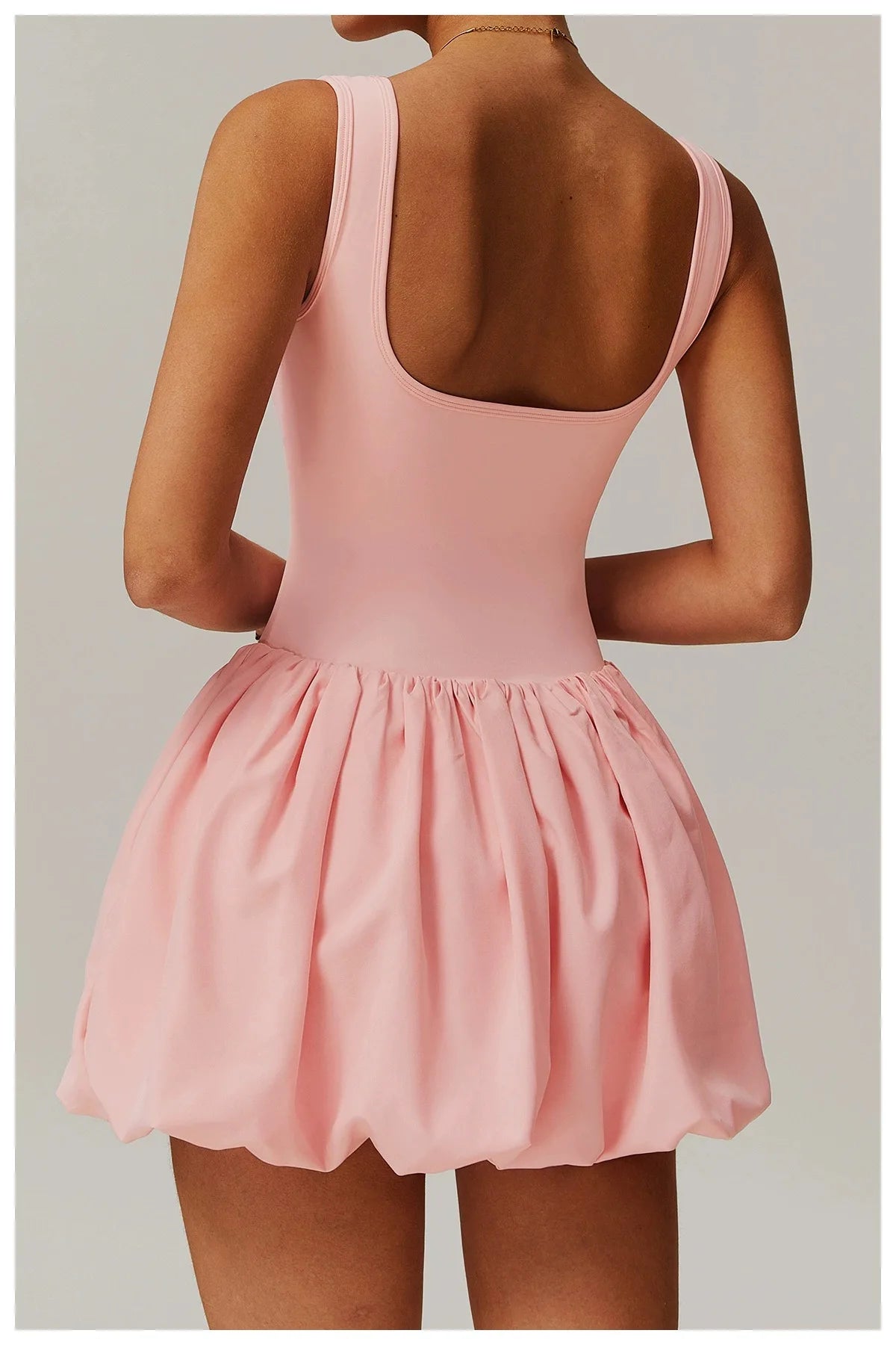 Model trägt ein pinkes Performance-Tenniskleid mit ärmellosem Oberteil und ausgestelltem Rock, von hinten gezeigt.