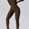 Model in a brown, long-sleeved half-zip yoga jumpsuit and white sneakers.