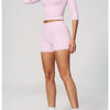 A woman models a pink two-piece yoga and fitness leggings set, consisting of a long-sleeved top and short bottoms.