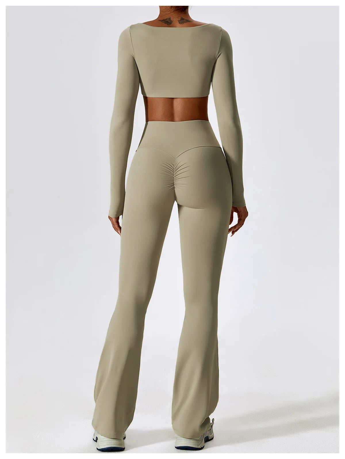 A model wears a seamless, long-sleeved performance tracksuit set in beige, featuring a cropped top and matching full-length p