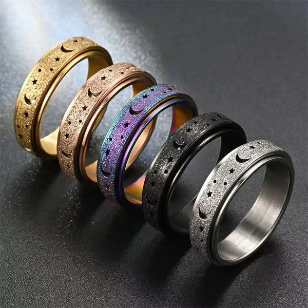 A row of stainless steel spinning rings featuring moon and star designs in gold, rose gold, and black finishes.