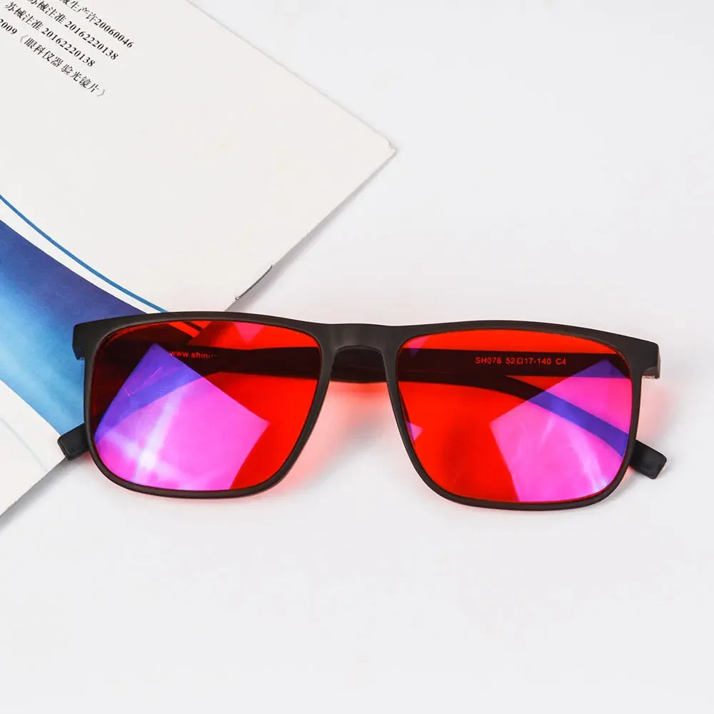 A pair of red tinted blue light blocking glasses resting on a white surface.