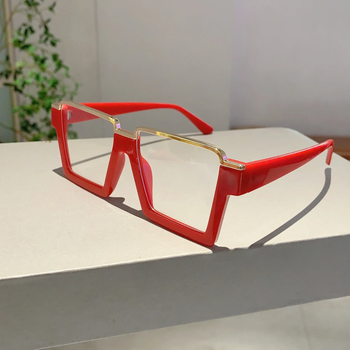 A pair of bright red oversized square semi-rim metal eyeglasses resting on a white surface.