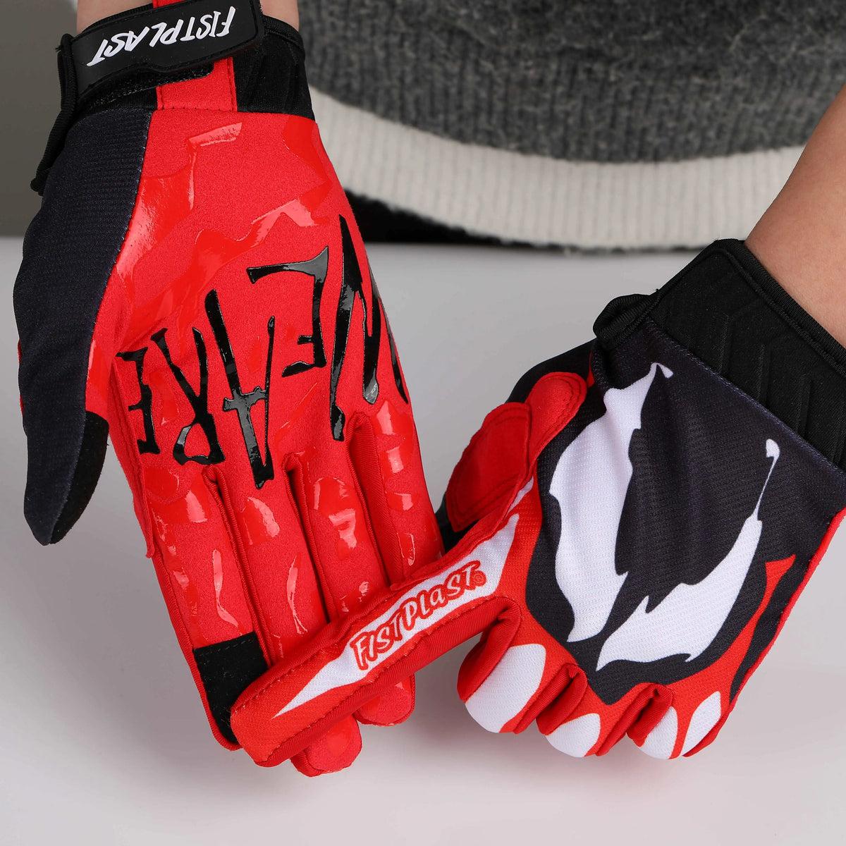 A pair of red and black cycling riding gloves are shown against a light gray background.