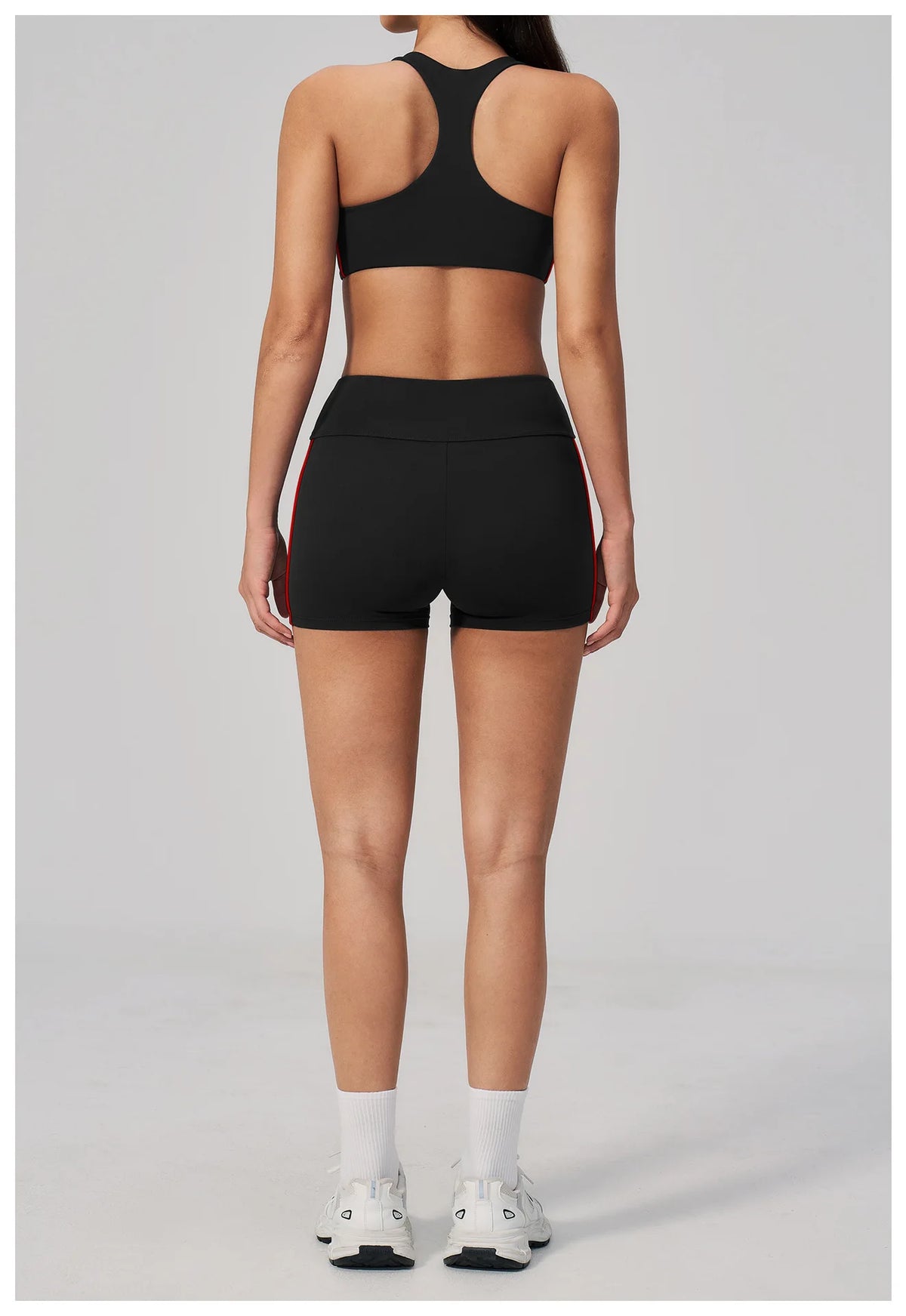 A woman models a black two-piece yoga and sports tracksuit set consisting of a cropped top and shorts.