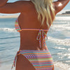 A woman wearing an elegant two-piece swimsuit set with colorful geometric patterns by the ocean.