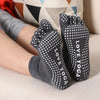 A pair of grey yoga socks with white polka dots are shown on a person's foot.