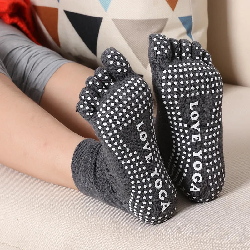 A pair of grey yoga socks with white polka dots are shown on a person's foot.