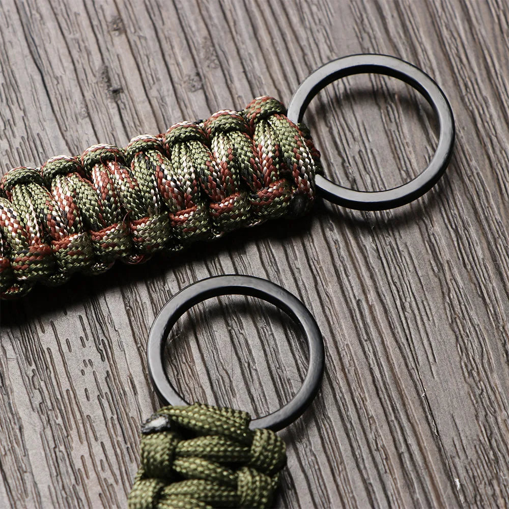 A close-up of a multi-tool keychain featuring a green and red braided cord attached to two black rings.
