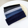 A stack of five black, gray, blue, and navy elastic hairbands is displayed on a light plate.