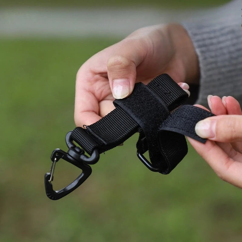A hand holds a black tactical nylon glove hook for storage and climbing.