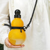 Eine Hand hält eine gelbe, kürbisförmige Sportflasche mit schwarzem Trageriemen vor einem weißen Stoffhintergrund.