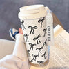 A white double-wall insulated stainless steel travel mug with a black bow pattern is held by a person.
