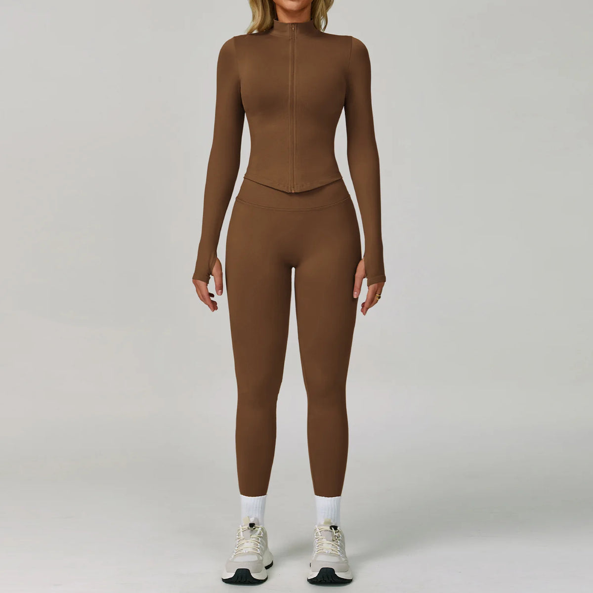 Eine Frau trägt einfarbige braune Langarm-Oberteil und Leggings mit weißen Socken und grauen Sportschuhen.