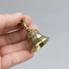 Une main tient une petite cloche de bronze antique avec un dessus orné et une base évasée.