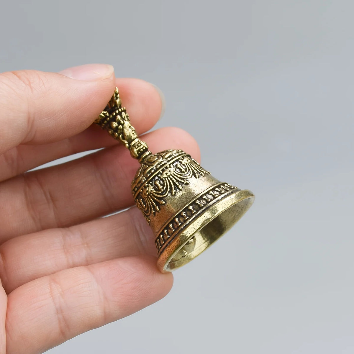 Une main tient une petite cloche de bronze antique avec un dessus orné et une base évasée.