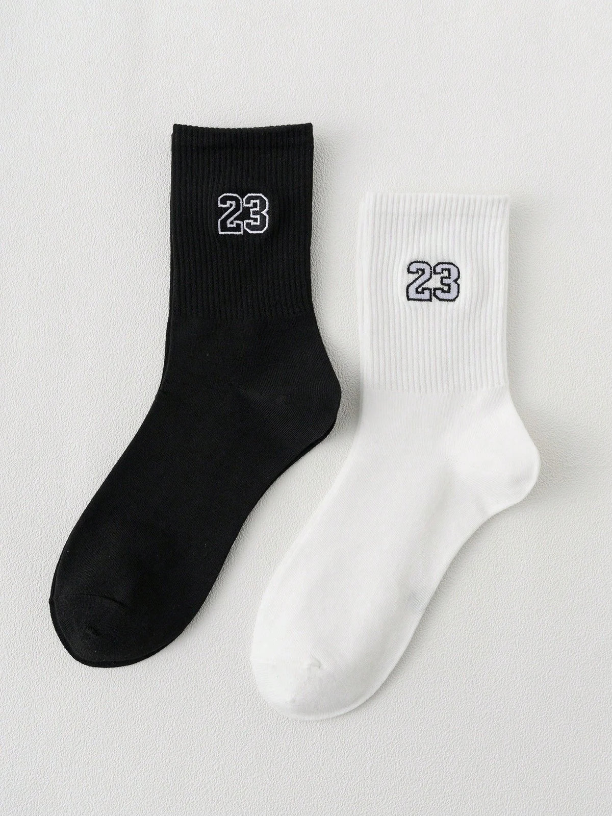 A pair of black and white crew socks featuring the number 23 on the foot.