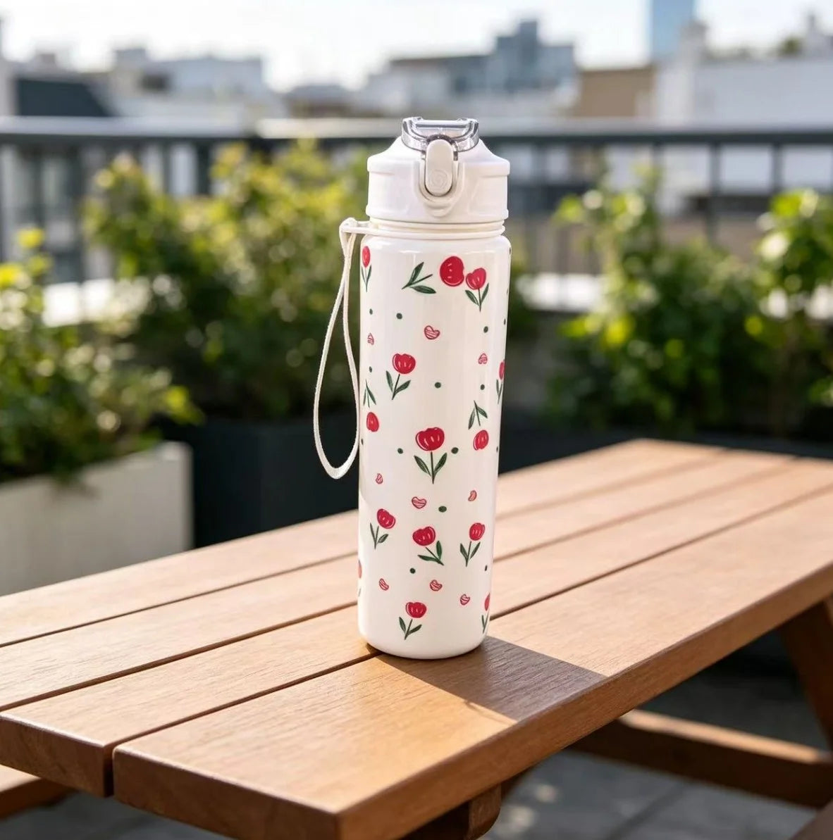 A white reusable strawberry bow water bottle standing on a wooden table outdoors.