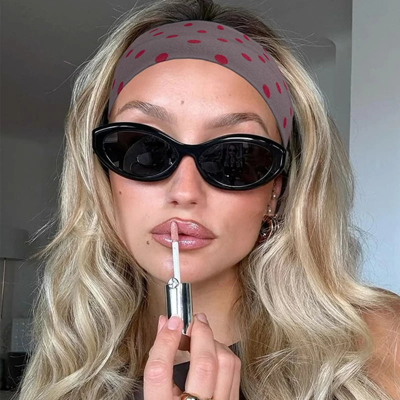 امرأة ترتدي ربطة رأس من قماش منقّط أسود وهي تمسك بجهاز فيب فضي.