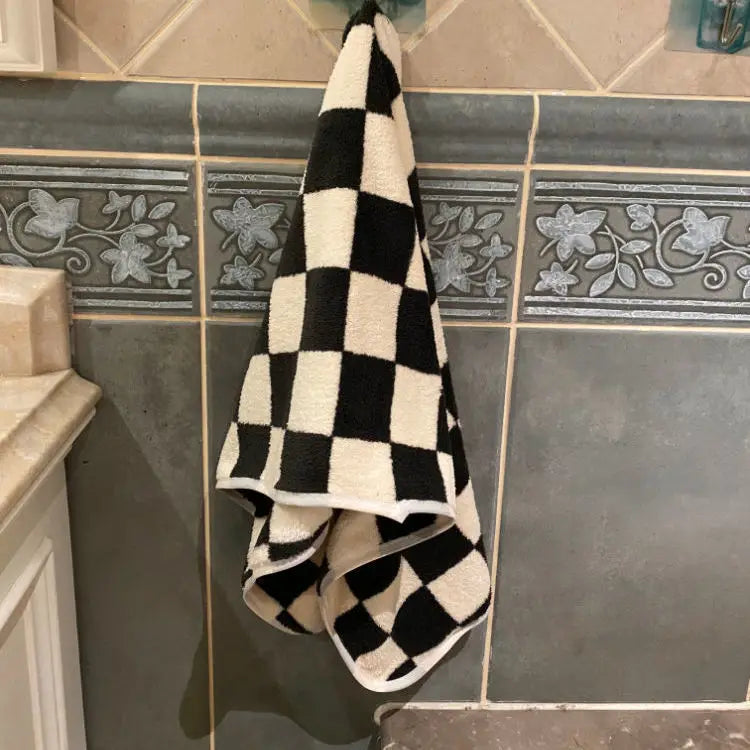 A black and white checkered face towel hanging on a tiled wall.