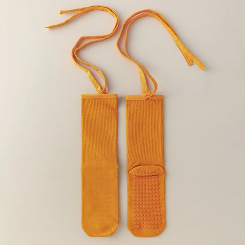 A pair of orange silicone anti-slip yoga socks with yellow ties.