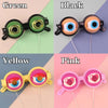 Four novelty glasses in green, black, yellow, and pink with various eye designs.